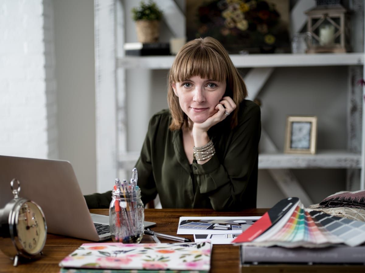 A woman at a desk with a laptop, fabric swatches and sketchbooks